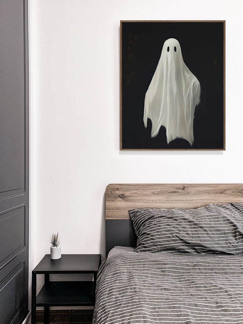 Peut inclure: Une peinture encadr&eacute;e repr&eacute;sentant un fant&ocirc;me blanc avec deux yeux noirs est accroch&eacute;e &agrave; un mur blanc au-dessus d'un lit avec une housse de couette ray&eacute;e gris et blanc.