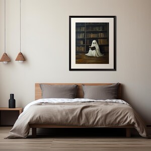 May include: A framed painting of a white ghost sitting in a library, reading a book. The ghost is wearing a white sheet and has a book in its hands. The library is filled with bookshelves and books.