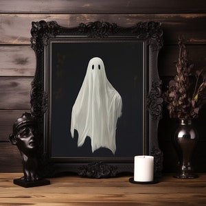 Peut inclure: Une image encadr&eacute;e en noir avec un fant&ocirc;me blanc au centre. Le fant&ocirc;me a deux yeux noirs et porte un drap blanc. L'image est pos&eacute;e sur une table en bois avec une bougie blanche et un vase de fleurs s&eacute;ch&eacute;es.