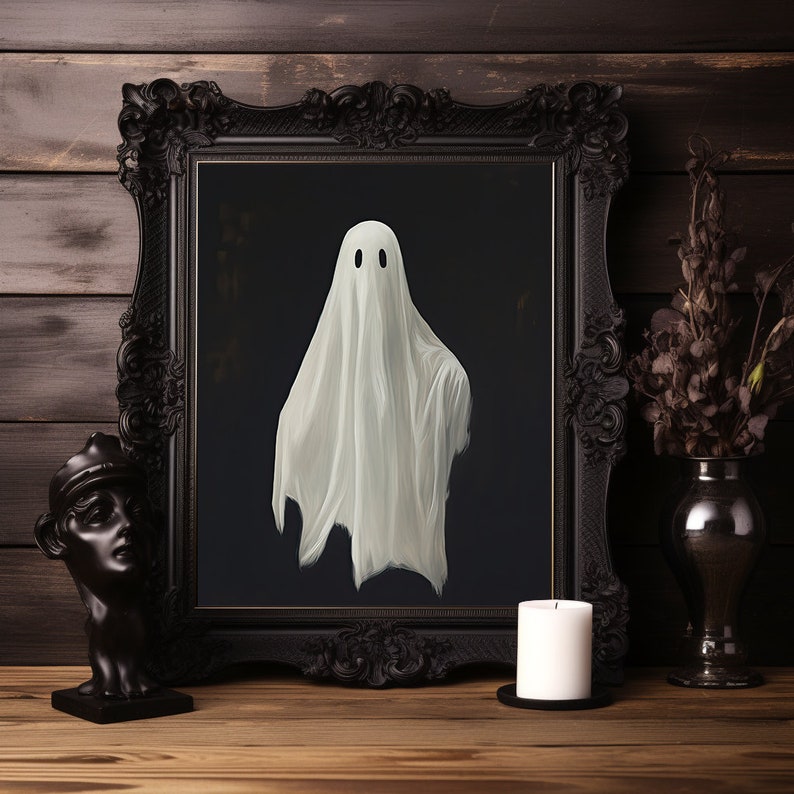 Peut inclure: Une image encadr&eacute;e en noir avec un fant&ocirc;me blanc au centre. Le fant&ocirc;me a deux yeux noirs et porte un drap blanc. L'image est pos&eacute;e sur une table en bois avec une bougie blanche et un vase de fleurs s&eacute;ch&eacute;es.