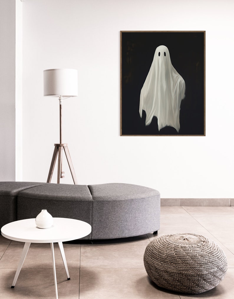 Peut inclure: Un fant&ocirc;me blanc avec deux yeux noirs est peint sur une toile noire. La toile est encadr&eacute;e dans un cadre en bois fonc&eacute; et est accroch&eacute;e &agrave; un mur blanc.