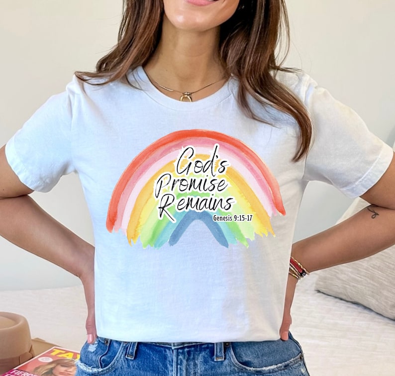 Pu&ograve; includere: Una maglietta bianca con un design arcobaleno e il testo "God's Promise Remains" con il riferimento biblico "Genesi 9:15-17".