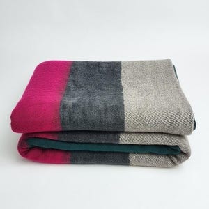 May include: Folded blanket with a color block design. The top blanket features a magenta stripe, followed by a dark gray and a light gray stripe. The second blanket has a teal stripe. The blankets are stacked on a white background.