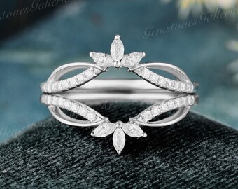 May include: A delicate silver ring with a marquise-shaped diamond setting. The ring features a double band with smaller diamonds set along the sides.