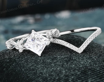 May include: A silver engagement ring set with a square-cut center stone and a delicate floral design. The matching wedding band features a V-shaped design with small diamonds.