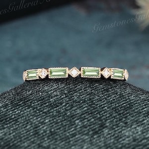 May include: A delicate gold band ring with a row of small, rectangular green gemstones and tiny round diamonds.