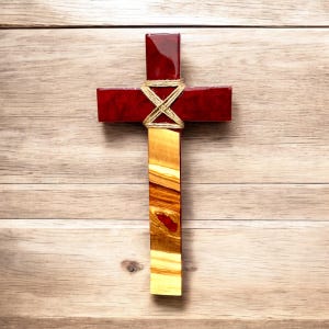 Puede incluir: Una cruz de madera con un acabado teñido de rojo y un patrón de veta de madera natural. La cruz está atada con cuerda en el centro.