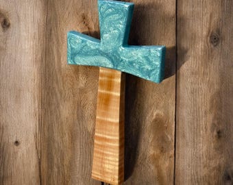 May include: A wooden cross with a teal blue epoxy resin inlay. The cross is mounted on a wooden wall.