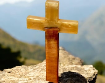 May include: A wooden cross with a yellow top and a brown base. The cross is standing on a rock with a blurry background of mountains.