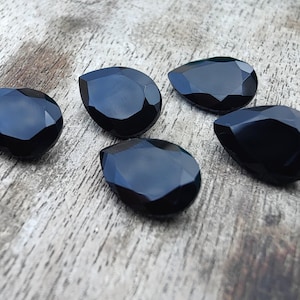 May include: Five black teardrop-shaped crystal beads. The beads are faceted and have a glossy finish.