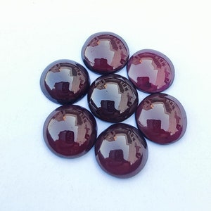 Puede incluir: Siete piedras preciosas redondas de color púrpura oscuro con un acabado brillante. Las piedras preciosas están dispuestas en círculo sobre un fondo blanco.