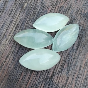 May include: Four light green, translucent, oval-shaped stones on a dark brown wooden surface.