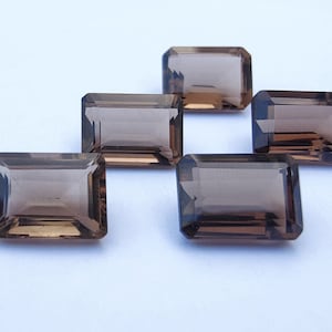 Puede incluir: Cinco piedras preciosas de cuarzo ahumado, talladas en forma de esmeralda rectangular, dispuestas en forma de espiga sobre una superficie blanca.