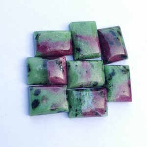 May include: A group of eight rectangular green and pink gemstones with black flecks. The gemstones are arranged in a loose pile.