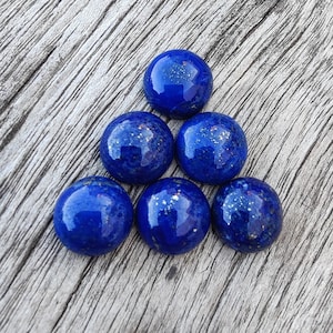 Könnte beinhalten: Sieben runde, blaue Lapislazuli-Cabochons mit goldenen Flecken. Die Cabochons sind in Dreiecksform angeordnet.