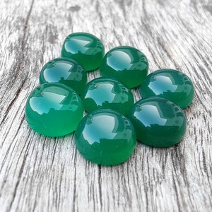May include: Eight round, green gemstone cabochons, likely agate, arranged in a circle on a wooden surface.