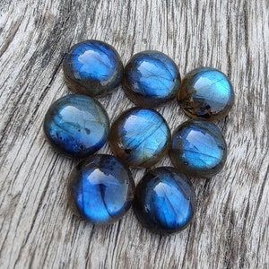 May include: Eight iridescent blue and grey labradorite gemstone cabochons, each with a unique pattern of inclusions, arranged in a circular pattern on a wooden surface.
