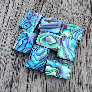 Pode incluir: Uma coleção de azulejos de concha de abalone iridescente em vários tons de azul e verde. Os azulejos são dispostos em um padrão escalonado, criando um mosaico visualmente atraente.