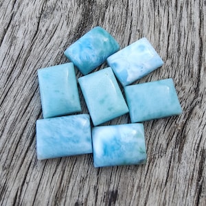 Puede incluir: Una colección de siete piedras de jaspe de mar azul claro y blanco, cada una cortada en forma rectangular. Las piedras están dispuestas sobre una superficie de madera.