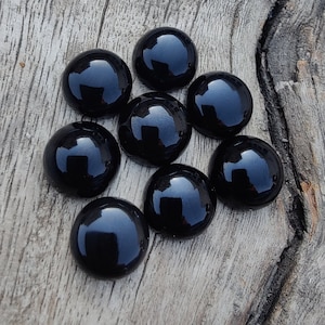 以下が含まれることがあります： 木製の背景に、滑らかで光沢のある表面を持つ黒いガラスのcabochonsが9つ、クラスター状に配置されています