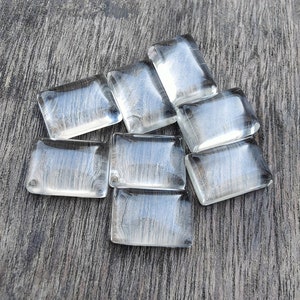 May include: A group of ten clear glass rectangular tiles with a frosted, textured surface. The tiles are arranged in a random pattern on a wooden surface.