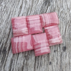 May include: Six pink and white striped rectangular stones, also known as pink calcite, on a wooden surface.