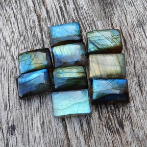 May include: A collection of eight iridescent labradorite gemstone cabochons in various shades of blue, green, and gold. The stones are cut into rectangular shapes and have a smooth, polished finish.