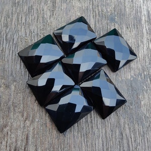 Puede incluir: Siete piedras preciosas cuadradas facetadas negras sobre una superficie de madera.