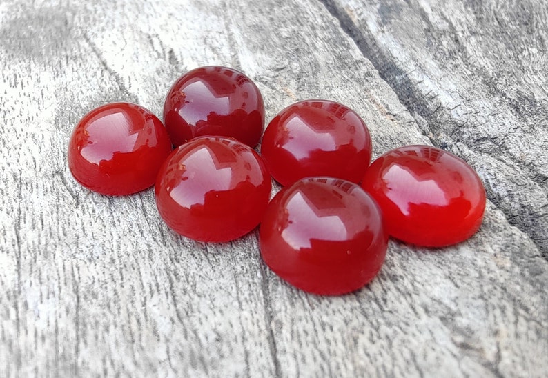 K&ouml;nnte beinhalten: Sechs runde, rote Cabochonsteine auf einer Holzoberfl&auml;che.