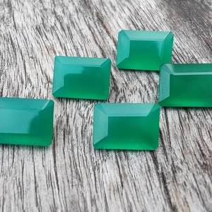 May include: Five green gemstone cabochons in a rectangular shape, displayed on a wooden surface.