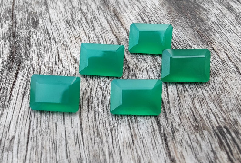 May include: Five green gemstone cabochons in a rectangular shape, displayed on a wooden surface.