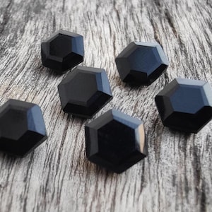 May include: Six black hexagonal buttons with a glossy finish. The buttons are arranged on a wooden surface.