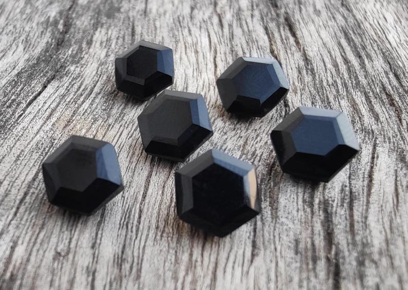 May include: Six black hexagonal buttons with a glossy finish. The buttons are arranged on a wooden surface.