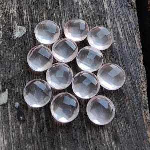 May include: A group of 12 round, faceted, pale pink rose quartz cabochons. The stones are smooth and translucent, with a slight shimmer.