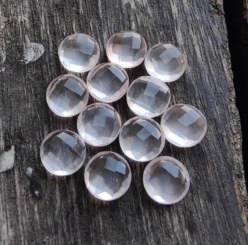 May include: A group of 12 round, faceted, pale pink rose quartz cabochons. The stones are smooth and translucent, with a slight shimmer.