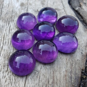 May include: Eight round, purple amethyst gemstones on a wooden surface.