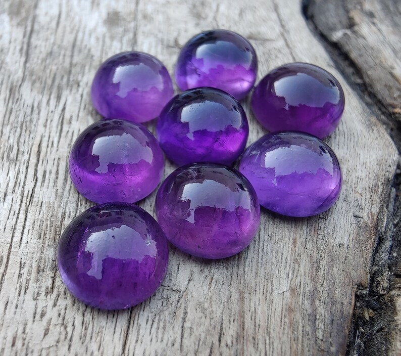 May include: Eight round, purple amethyst gemstones on a wooden surface.