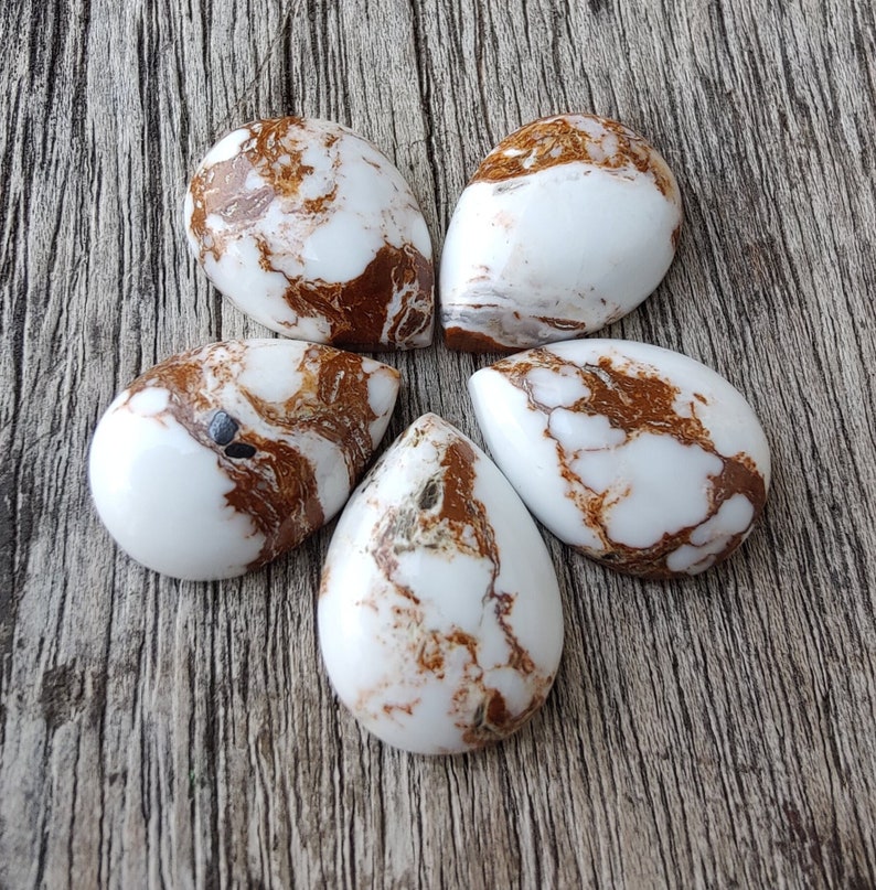 Puede incluir: Cinco cabujones en forma de l&aacute;grima de &aacute;gata blanca y marr&oacute;n. Las piedras tienen un patr&oacute;n de remolino de blanco y marr&oacute;n.