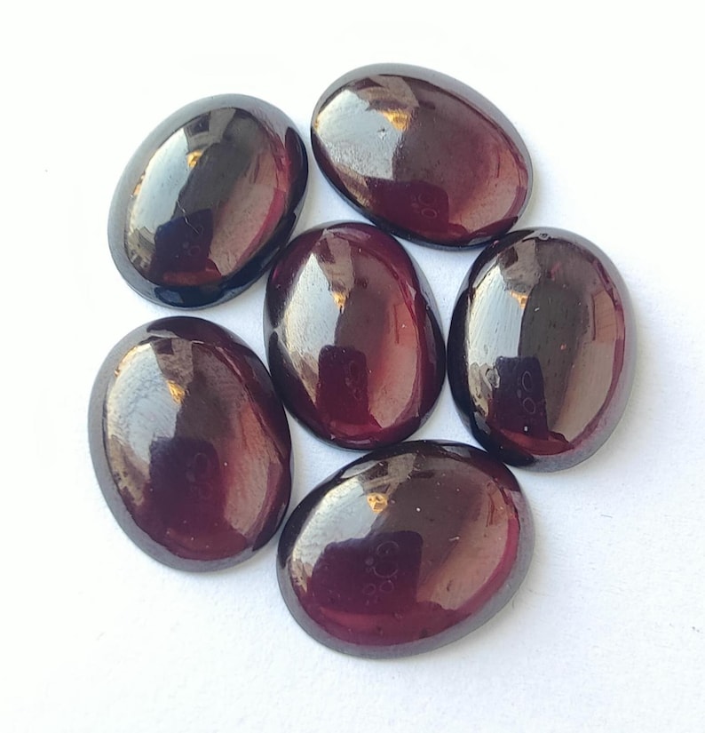 Puede incluir: Seis piedras preciosas ovaladas de color rojo oscuro con un acabado brillante. Las piedras preciosas est&aacute;n dispuestas en forma circular.