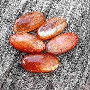 K&ouml;nnte beinhalten: F&uuml;nf glatte, ovalf&ouml;rmige Sunstone-Steine in Orange- und Goldt&ouml;nen. Die Steine haben eine schimmernde, irisierende Qualit&auml;t.