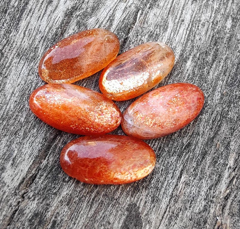 K&ouml;nnte beinhalten: F&uuml;nf glatte, ovalf&ouml;rmige Sunstone-Steine in Orange- und Goldt&ouml;nen. Die Steine haben eine schimmernde, irisierende Qualit&auml;t.