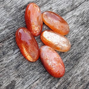 K&ouml;nnte beinhalten: F&uuml;nf ovale, getrommelte Sunstone-Steine in rot-orange mit schimmerndem, irisierendem Finish.