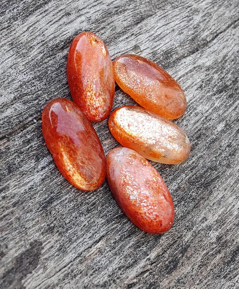 K&ouml;nnte beinhalten: F&uuml;nf ovale, getrommelte Sunstone-Steine in rot-orange mit schimmerndem, irisierendem Finish.
