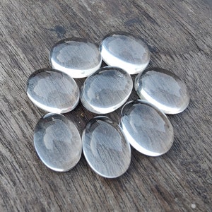 May include: Eight clear glass stones, oval shaped, arranged in a circle on a wooden surface.