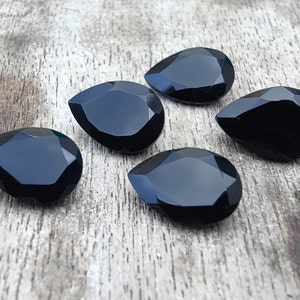 May include: Five black teardrop-shaped faceted glass gems on a wooden surface.