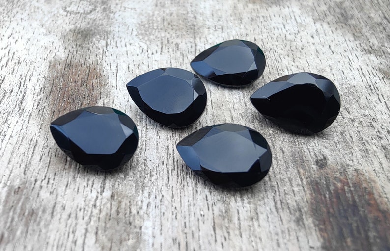May include: Five black teardrop-shaped faceted glass gems on a wooden surface.