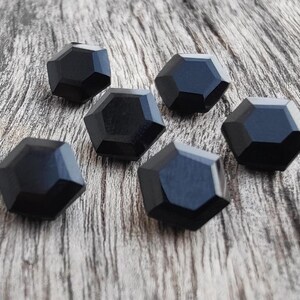 May include: Six black, faceted, geometric buttons. The buttons are arranged in a semi-circle on a wooden surface.