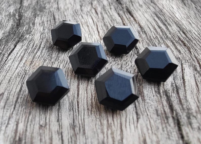 May include: Six black, faceted, geometric buttons. The buttons are arranged in a semi-circle on a wooden surface.