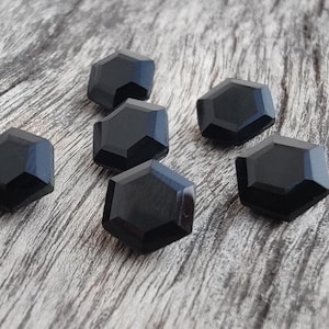 May include: Six black hexagonal buttons with a shiny finish. The buttons are arranged in a semi-circle on a wooden surface.