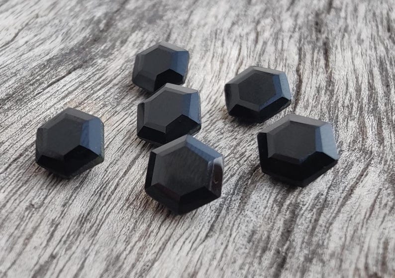 May include: Six black hexagonal buttons with a shiny finish. The buttons are arranged in a semi-circle on a wooden surface.